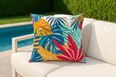 Colorful tropical leaf-patterned pillow on a white outdoor sofa near a pool.